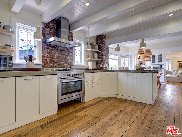 kitchen with hanging light fixtures, wall chimney exhaust hood, white cabinetry, and high end stainless steel range oven