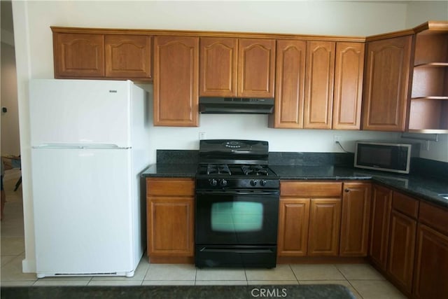 kitchen featuring dark stone counters, light tile patterned flooring, black gas range, and white fridge