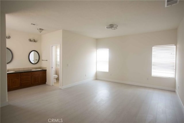 unfurnished room with a healthy amount of sunlight, sink, and light hardwood / wood-style floors