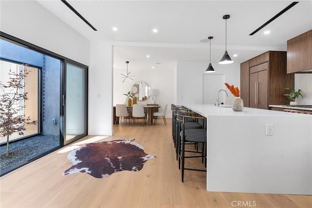 kitchen with pendant lighting, a breakfast bar, sink, light wood-type flooring, and paneled built in fridge