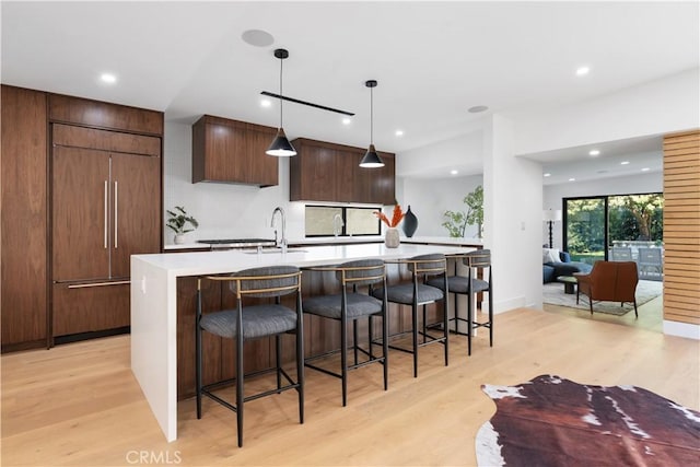 kitchen with pendant lighting, light hardwood / wood-style floors, sink, an island with sink, and paneled built in fridge