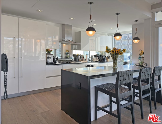 kitchen featuring wall chimney exhaust hood, pendant lighting, light hardwood / wood-style flooring, and white cabinets