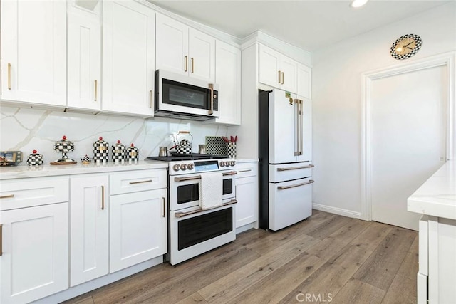 kitchen featuring white cabinets, backsplash, premium appliances, and light hardwood / wood-style floors