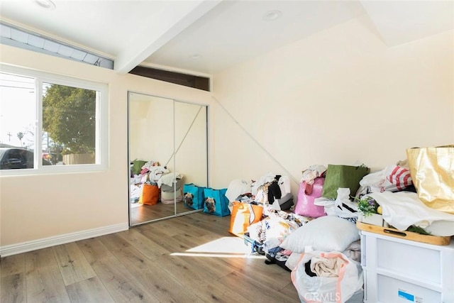 unfurnished bedroom with wood-type flooring, a closet, and lofted ceiling with beams