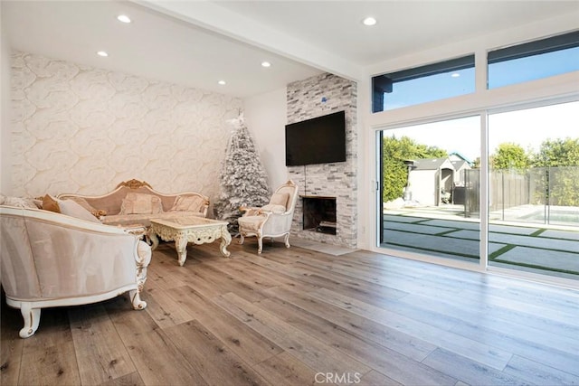 living room with beam ceiling, light hardwood / wood-style flooring, and a stone fireplace