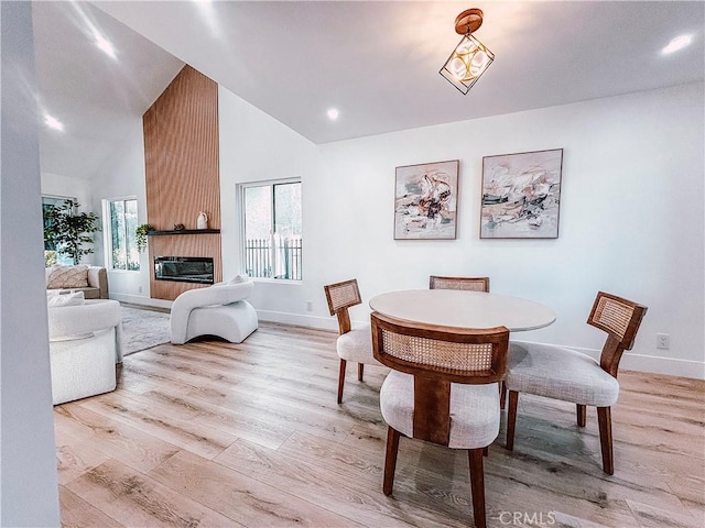 dining area featuring an inviting chandelier, a large fireplace, light hardwood / wood-style floors, and high vaulted ceiling