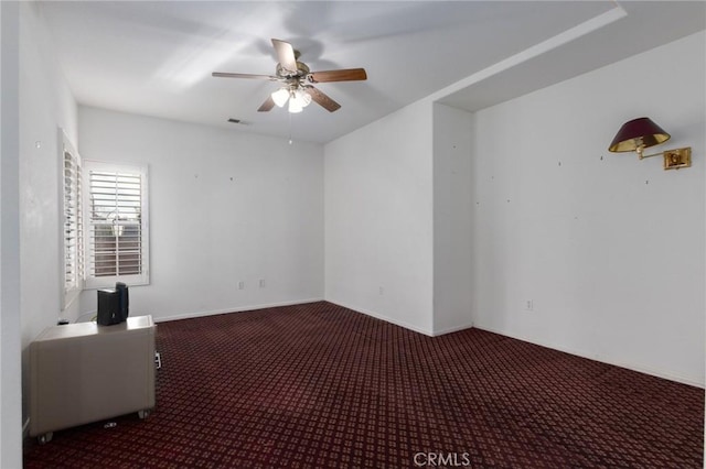 spare room featuring dark colored carpet and ceiling fan