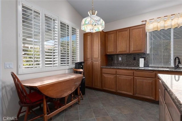 kitchen featuring lofted ceiling, dark stone countertops, decorative backsplash, sink, and hanging light fixtures