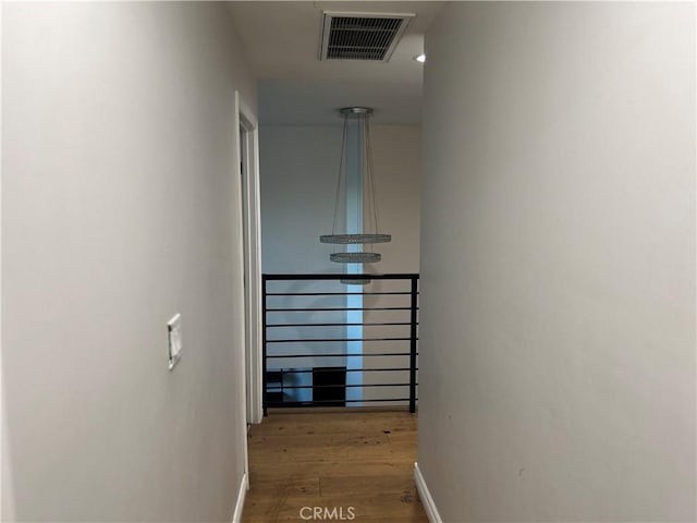 hall featuring baseboards, visible vents, and wood finished floors