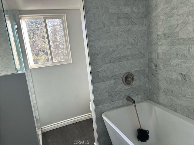 bathroom featuring a soaking tub, baseboards, and wood finished floors