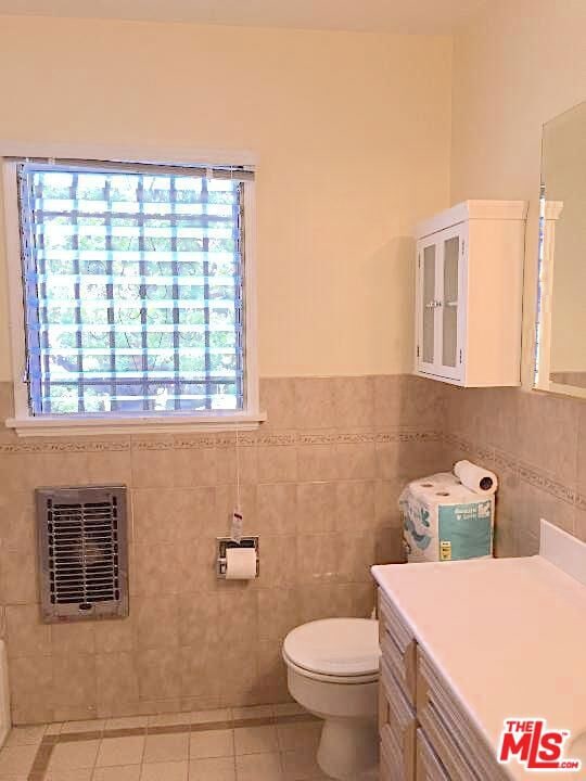 bathroom with toilet, tile walls, tile patterned floors, heating unit, and vanity