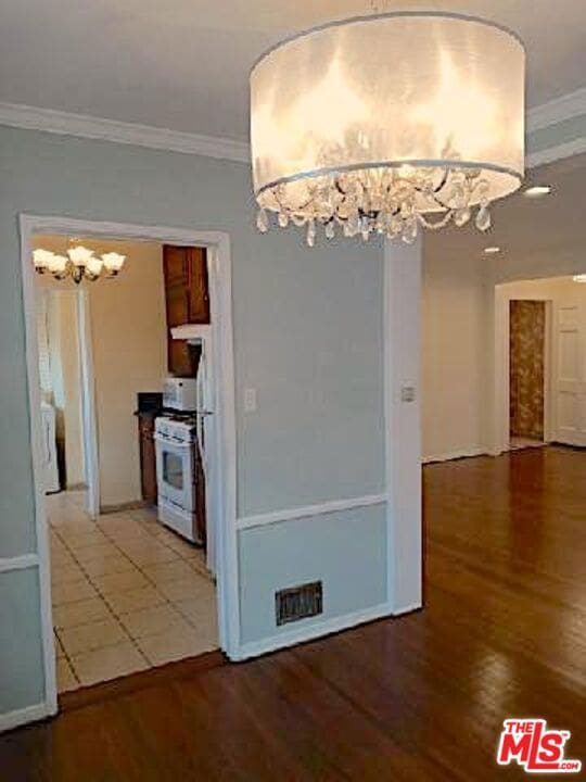 unfurnished dining area featuring crown molding, wood-type flooring, and an inviting chandelier