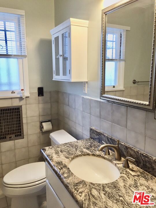 bathroom featuring toilet, a healthy amount of sunlight, tile walls, and vanity