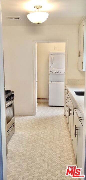 kitchen with white cabinets, stacked washer / dryer, sink, and stainless steel range with gas stovetop