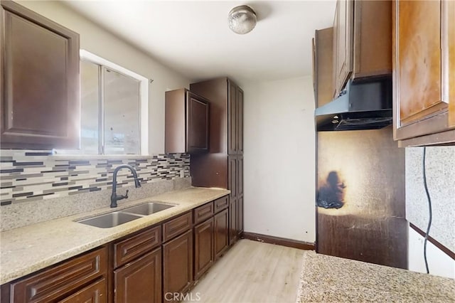 kitchen featuring light stone countertops, decorative backsplash, light hardwood / wood-style flooring, and sink