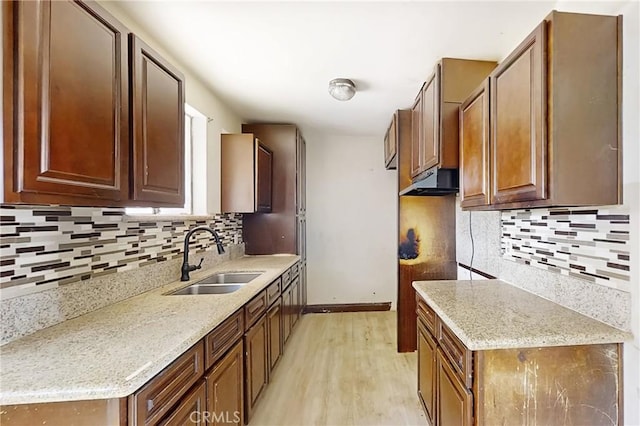 kitchen with tasteful backsplash, sink, light stone counters, and light hardwood / wood-style floors