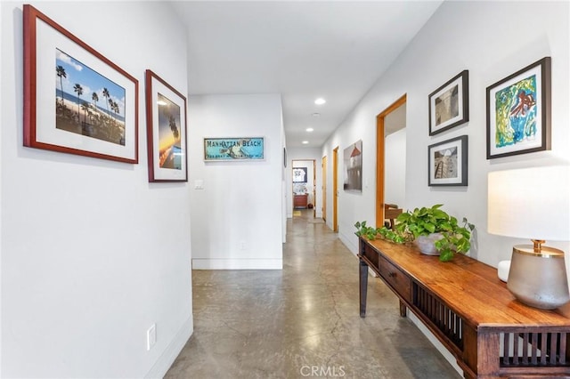 hall featuring concrete flooring, recessed lighting, and baseboards