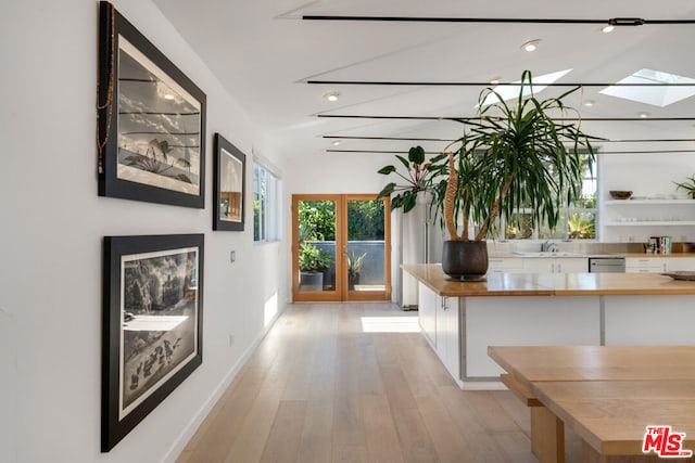 hallway featuring vaulted ceiling with skylight, light hardwood / wood-style flooring, and french doors