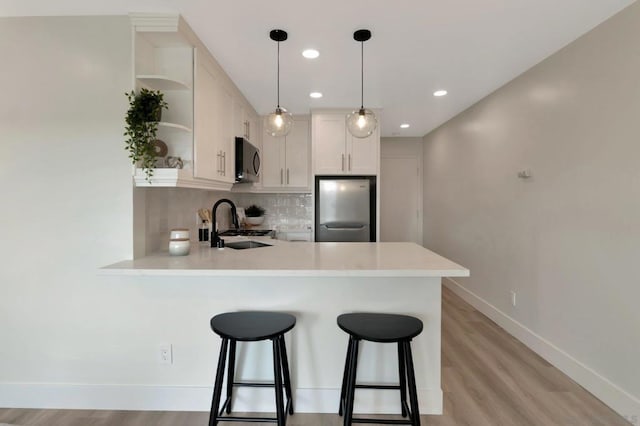 kitchen with white cabinetry, kitchen peninsula, stainless steel appliances, tasteful backsplash, and decorative light fixtures