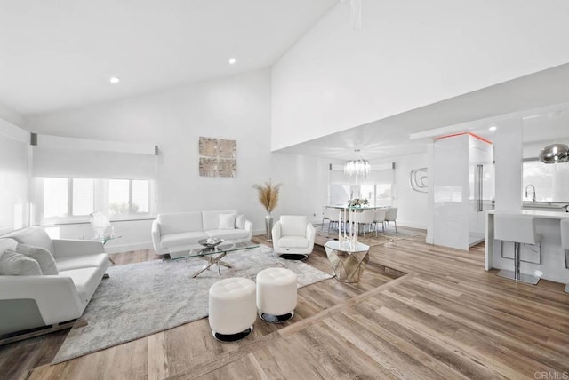 living room with high vaulted ceiling, sink, and light wood-type flooring