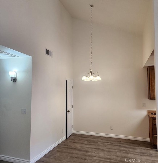 unfurnished dining area featuring high vaulted ceiling, dark wood-type flooring, and a chandelier