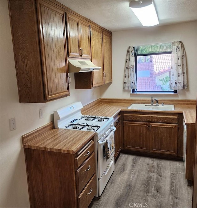 kitchen featuring white gas stove, under cabinet range hood, a textured ceiling, a sink, and wood finished floors