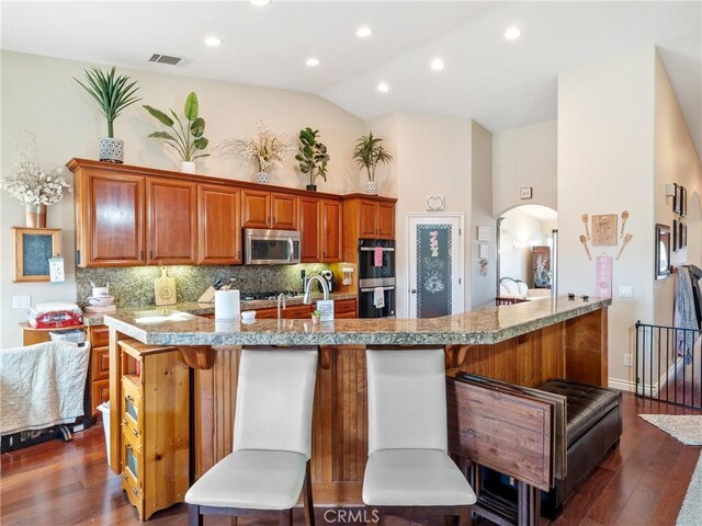 kitchen with a kitchen bar, stainless steel appliances, tasteful backsplash, dark hardwood / wood-style flooring, and vaulted ceiling