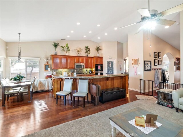 kitchen featuring a kitchen bar, stainless steel appliances, backsplash, dark wood-type flooring, and light stone counters