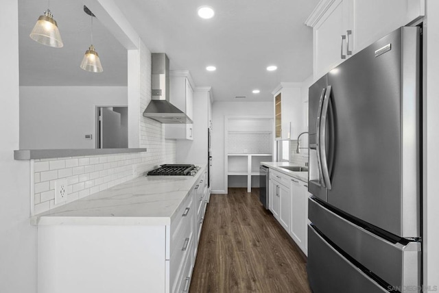 kitchen with appliances with stainless steel finishes, pendant lighting, white cabinets, wall chimney range hood, and sink