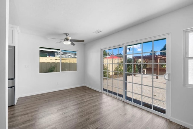 empty room with dark wood-type flooring, ceiling fan, and a wealth of natural light