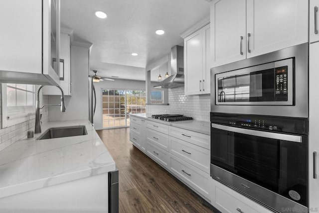 kitchen with wall chimney exhaust hood, dark hardwood / wood-style floors, stainless steel appliances, white cabinets, and sink