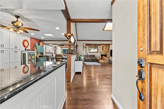 kitchen with white cabinetry, ceiling fan, dark wood-type flooring, dark stone countertops, and a fireplace