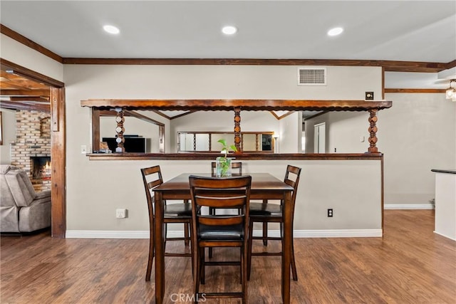 dining space featuring a brick fireplace, wood-type flooring, and crown molding