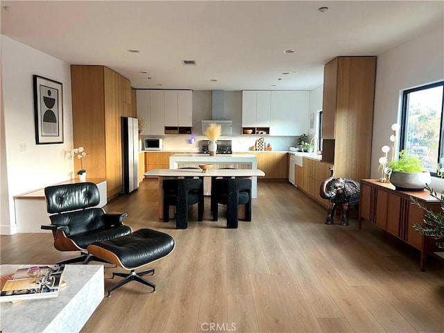 kitchen with sink, white cabinets, stainless steel appliances, light wood-type flooring, and wall chimney exhaust hood