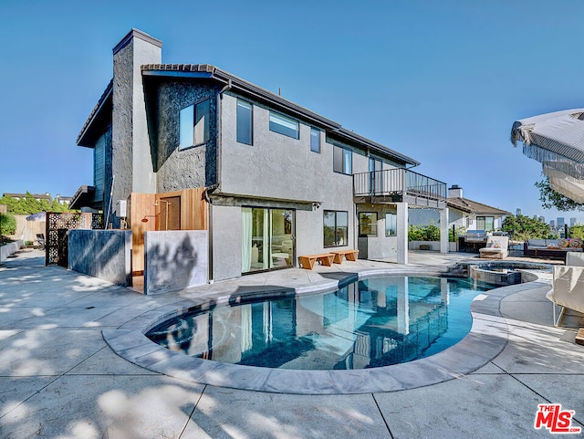 back of property featuring a swimming pool with hot tub, a patio, and a balcony