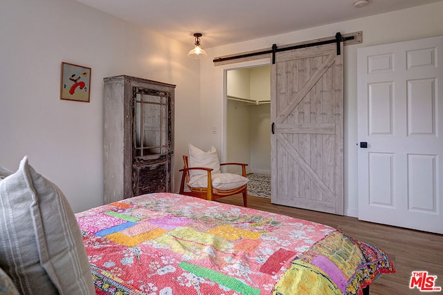 bedroom with a barn door, a spacious closet, dark hardwood / wood-style flooring, and a closet