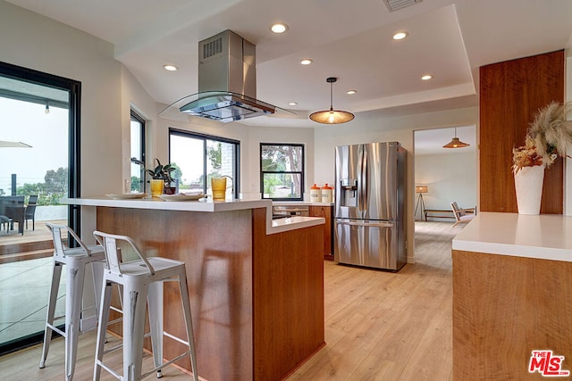 kitchen featuring island range hood, light hardwood / wood-style flooring, stainless steel fridge, pendant lighting, and a kitchen island with sink