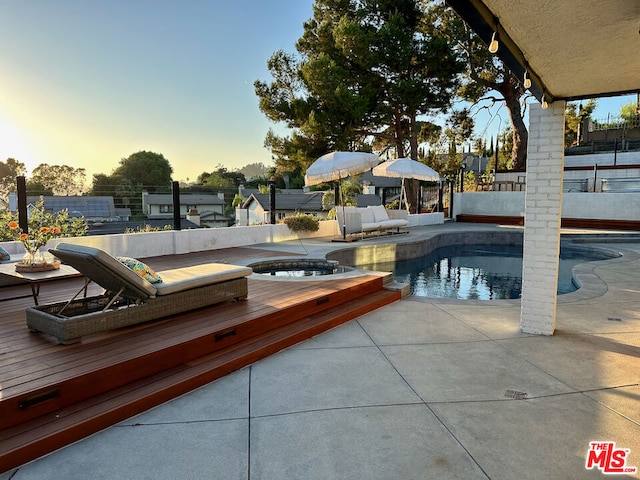 pool at dusk featuring an in ground hot tub and a patio