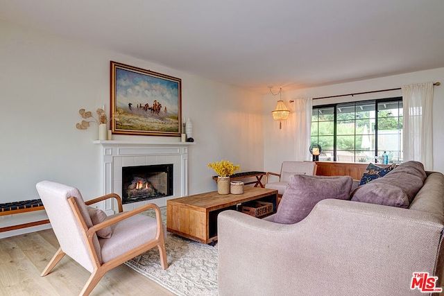 living room with a tiled fireplace and light wood-type flooring