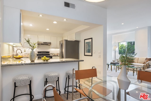 kitchen with black range with gas stovetop, kitchen peninsula, stainless steel refrigerator, light stone countertops, and white cabinets