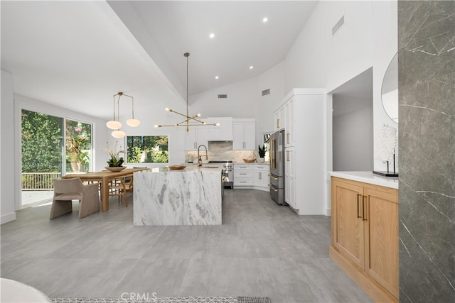 kitchen with light stone countertops, pendant lighting, white cabinets, an island with sink, and backsplash