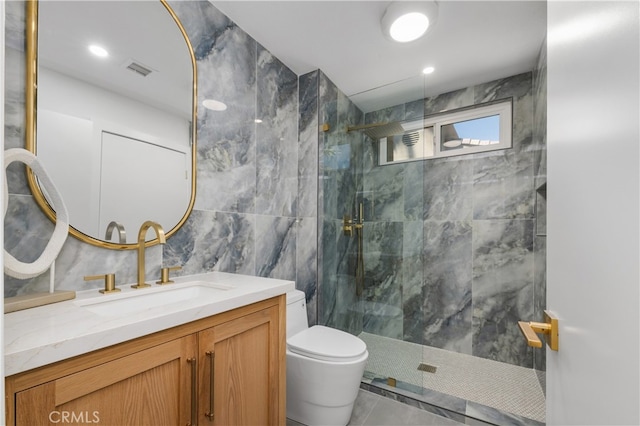 bathroom featuring tile patterned flooring, vanity, tile walls, toilet, and a tile shower