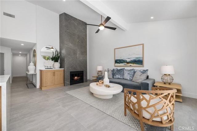 living room with a premium fireplace, ceiling fan, and beamed ceiling