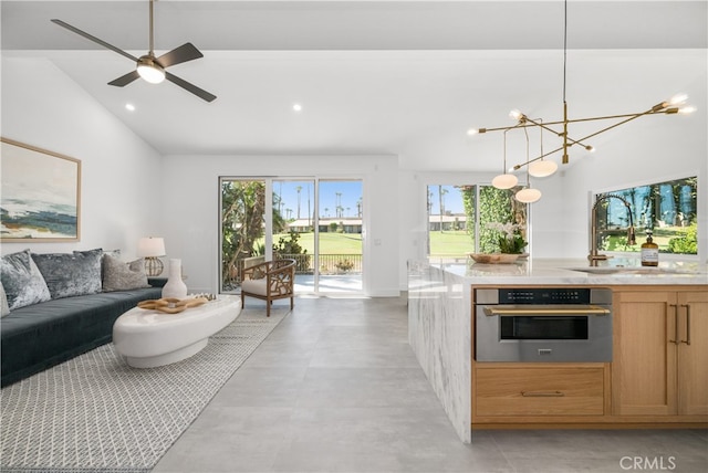 kitchen with lofted ceiling, oven, sink, hanging light fixtures, and ceiling fan with notable chandelier