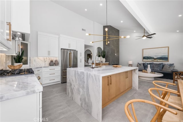 kitchen featuring white cabinets, an island with sink, light stone counters, and stainless steel appliances