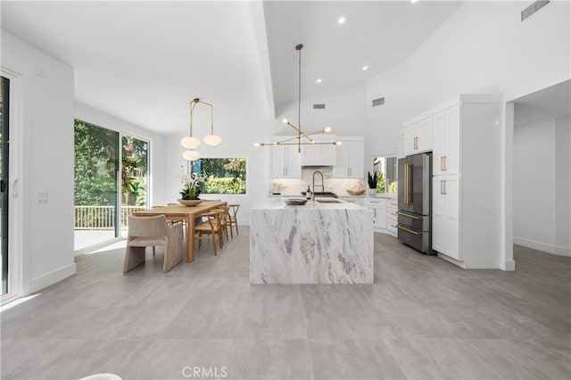 kitchen featuring light stone countertops, high quality fridge, decorative light fixtures, white cabinetry, and sink