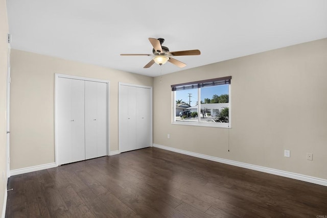 unfurnished bedroom with two closets, ceiling fan, and dark hardwood / wood-style floors