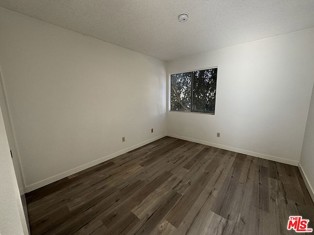 empty room with a textured ceiling and dark hardwood / wood-style floors