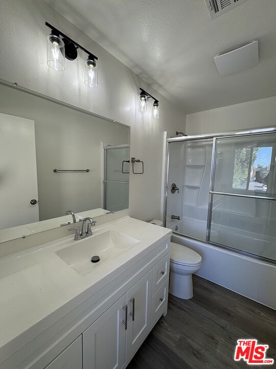 full bathroom featuring vanity, a textured ceiling, shower / bath combination with glass door, wood-type flooring, and toilet