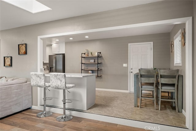 kitchen with stainless steel fridge with ice dispenser, light hardwood / wood-style floors, kitchen peninsula, a breakfast bar area, and white cabinets